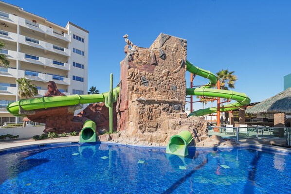 A swimming pool with a rock formation and green slides.