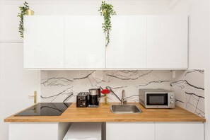 A kitchen with white cabinets, a marble backsplash, a wooden countertop, a coffee maker, a toaster, a sink, and two hanging plants. - Merveil - Family Suite - Marais - Saint Denis II (Paris)