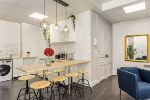 Una cocina moderna con una barra de madera, taburetes de bar, plantas colgantes, un microondas y un sofá azul.