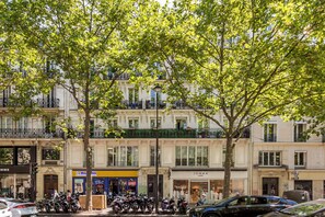 A street view with parked motorcycles, a row of shops, and multi-story buildings with balconies. - Merveil - Family Suite - Marais - Sebastopol III (Paris)