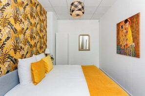 A hotel room with a bed, a large floral-patterned wall, a painting, and a ceiling light fixture. - Merveil - Family Suite - Marais - Sebastopol III (Paris)