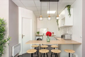 A modern kitchen with a central island, bar stools, hanging pendant lights, and a microwave. - Merveil - Family Suite - Marais - Sebastopol III (Paris)