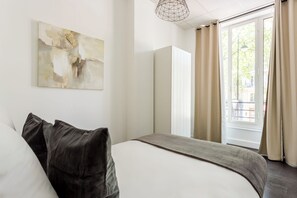 Una habitación de hotel moderna con una cama grande, una obra de arte minimalista en la pared y vistas de la ciudad a través de la ventana.