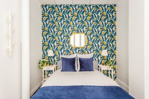 Un dormitorio con una cama, dos mesitas de noche, un espejo y un papel tapiz estampado.