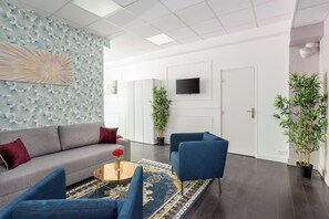 Una sala moderna con un sofá gris, sillones azules, una mesa redonda de centro con un jarrón de flores rojas y una alfombra estampada.