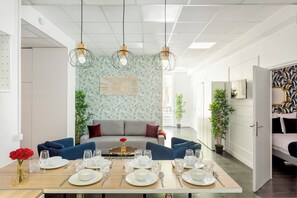 Un comedor con una larga mesa dispuesta para seis personas, un sofá al fondo y un muro con estampado.