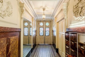 A hallway with ornate doors, patterned floor tiles, and a ceiling with decorative molding. - Merveil - Family Suite - Marais - Sebastopol III (Paris)