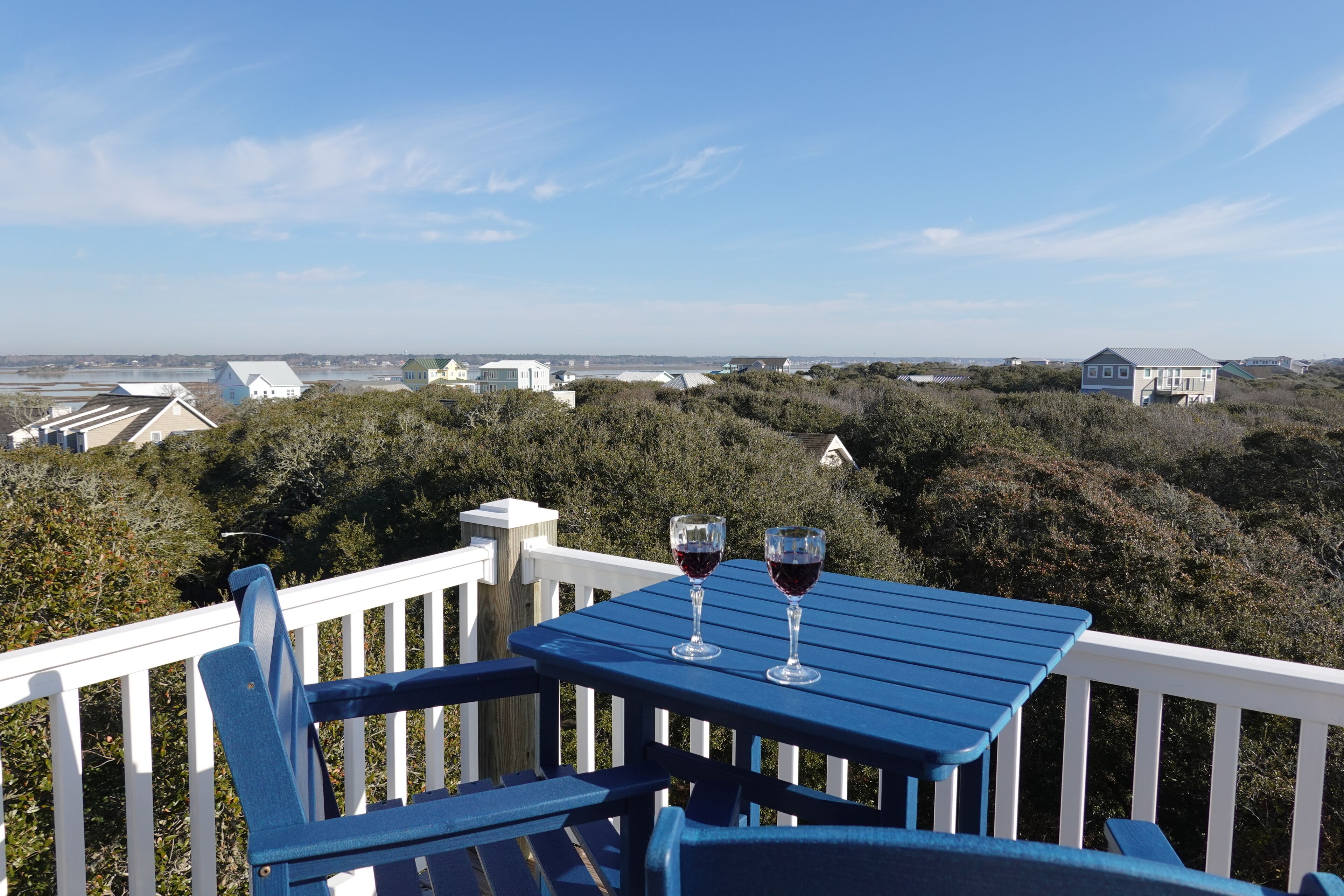 A blue deck with two wine glasses, overlooking a coastal landscape with houses and trees.