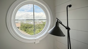 Habitación con ventanal circular que ofrece vistas a un puente y zonas verdes. Una lámpara de pie negra se encuentra a la derecha de la ventana.