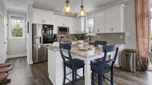 Una cocina moderna con armarios blancos, electrodomésticos de acero inoxidable, una isla de mármol y taburetes de bar azules.