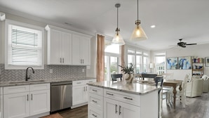 Cocina moderna con armarios blancos, lavavajillas de acero inoxidable y luces colgantes.