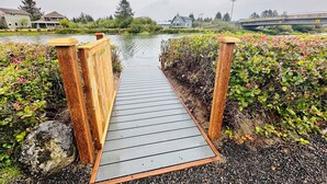 Un pont en bois enjambant un plan d’eau, avec des maisons et un autre pont visibles au loin.