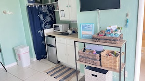 Une petite cuisine équipée d’un four à micro-ondes, d’un évier et de placards de rangement. On y trouve également une petite poubelle, un tapis à rayures et un panneau d’accueil.