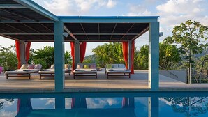 Zona de piscina con sillas de descanso y un espacio de estar techado.