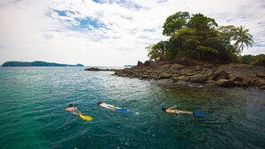 Three people swimming in a clear blue sea with a rocky shore and a tree-covered island in the background. - VIP amazing private island (Veraguas)