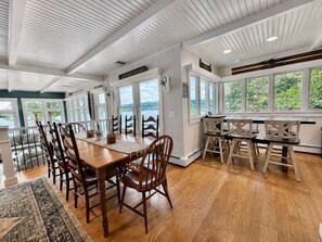 A dining area with a wooden table and chairs, large windows, and a view of the outdoors. - Lake Winni- Amazing waterfront oasis- beach, dock and more! (Laconia)