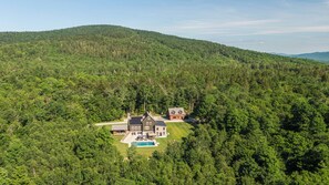 Una casa grande con piscina, rodeada de un bosque denso y colinas.