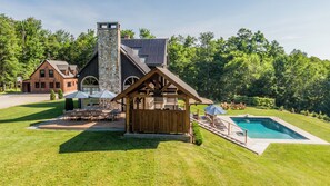 A lodge with a stone chimney, a pool, and outdoor seating.