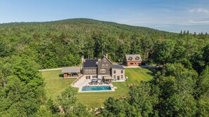 Una casa grande con piscina, rodeada de un césped cuidado y un bosque frondoso.