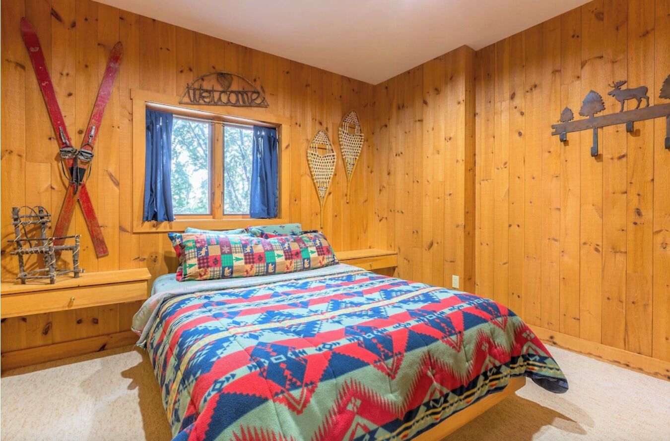 Una habitación con paneles de madera, una cama, una ventana con cortinas y equipo de esquí en la pared.