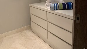 Een compacte badkamer met een witte wastafel, een handdoek en een plank met een opgevouwen plaid.