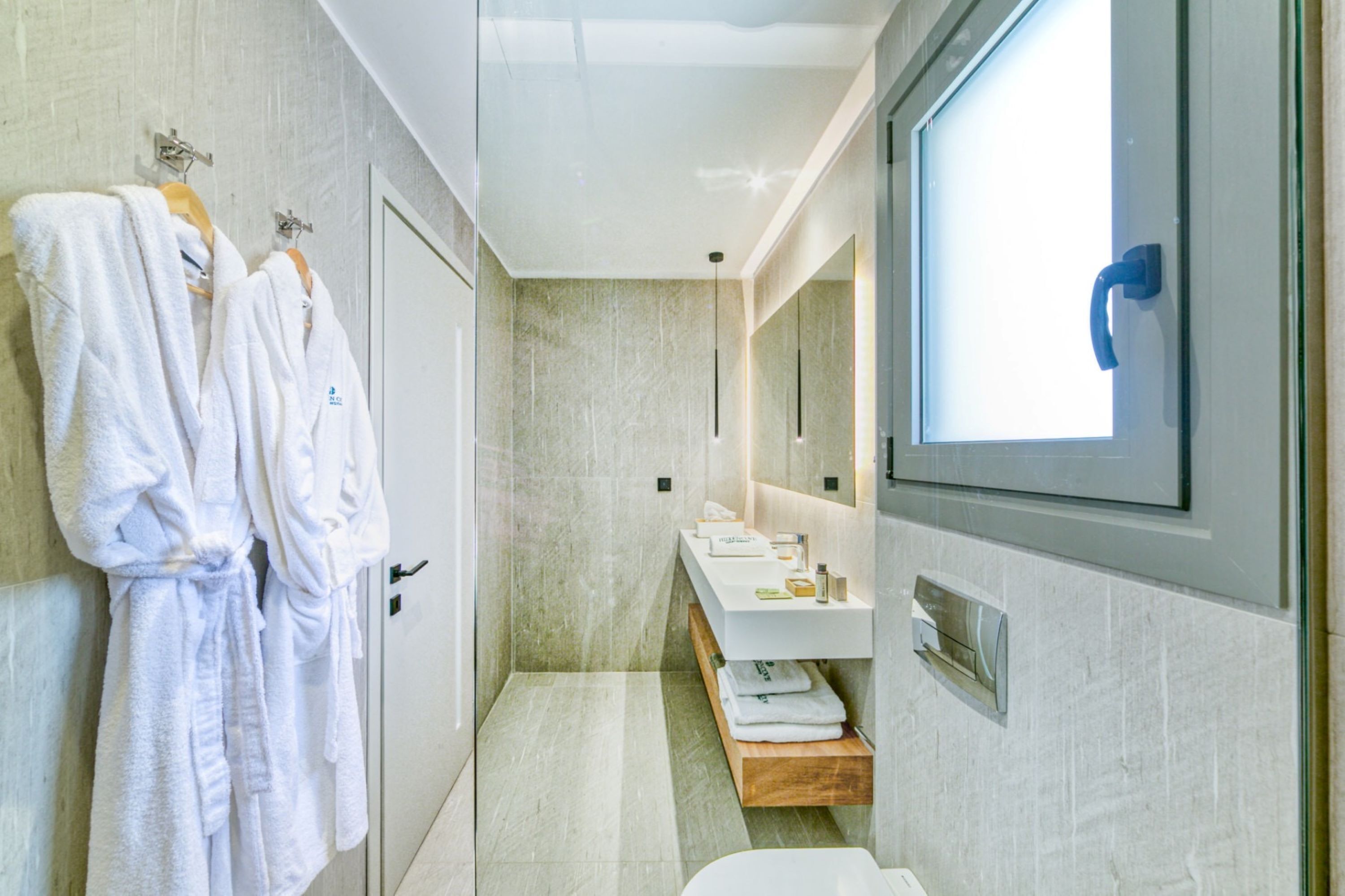 A modern bathroom with a large mirror, a vanity with a sink, and two white robes hanging on a rack.
