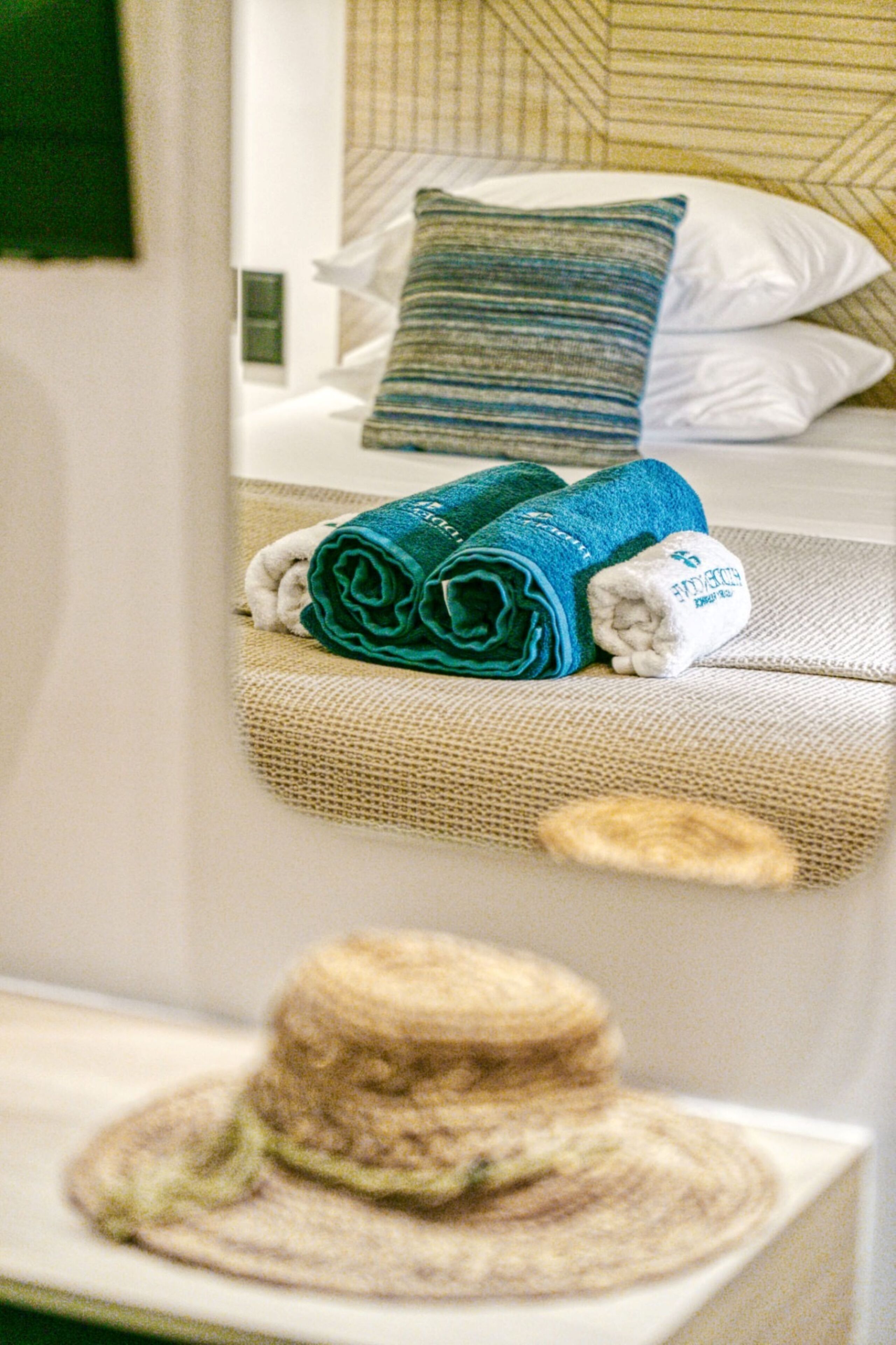 A neatly made bed with a blue and white striped pillow, a rolled-up towel, and a white pillow with a logo.