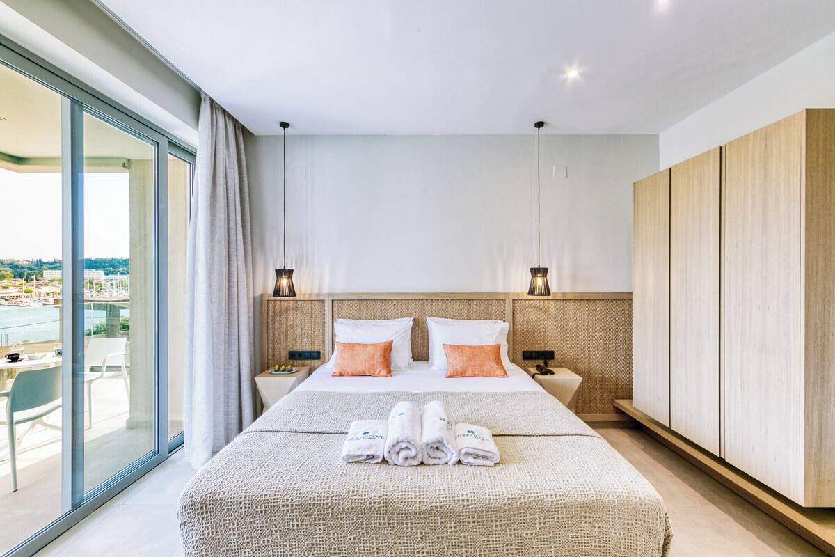 Quarto de hotel moderno com uma cama grande, duas mesas de cabeceira, um guarda-roupa e uma varanda com vista.