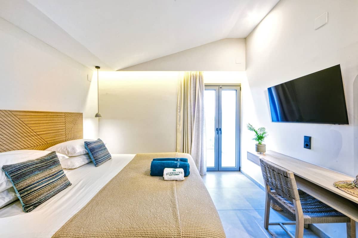 Quarto de hotel com cama, televisão presa à parede, mesa pequena e uma cadeira.