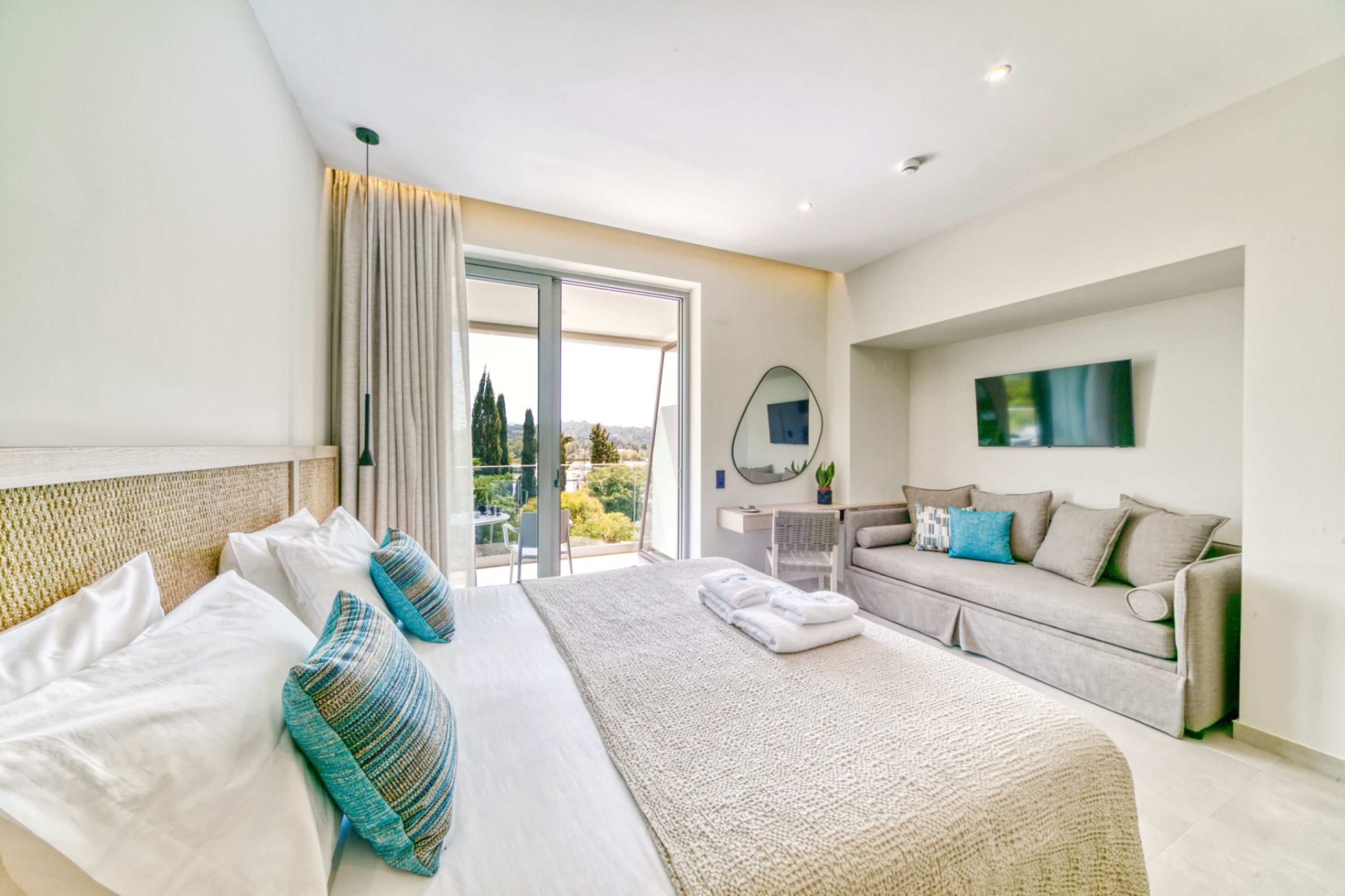 Una habitación de hotel moderna con una cama grande, un sofá, un balcón con vistas y un televisor de pantalla plana.