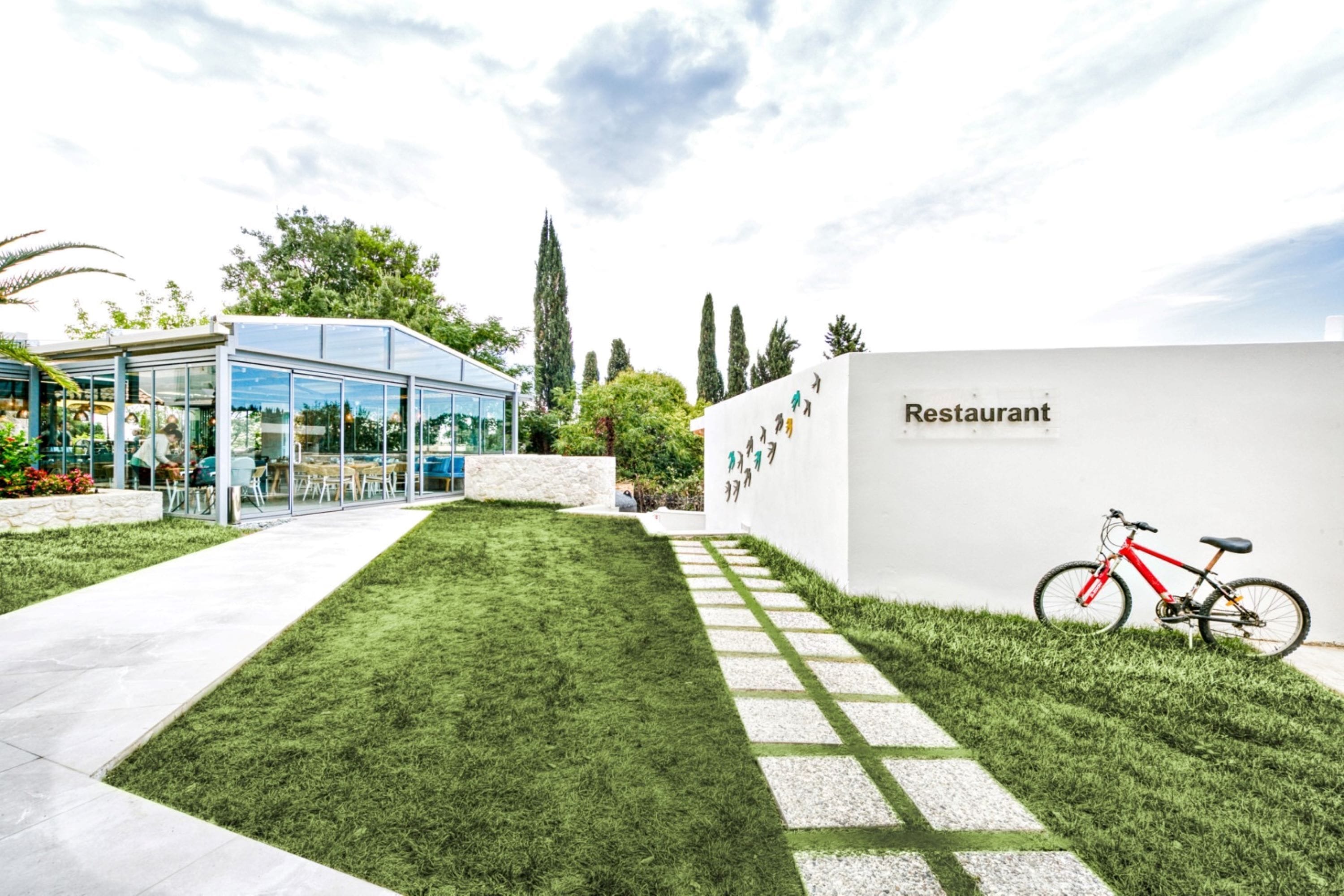 A modern restaurant with a glass facade, a neatly trimmed lawn, and a red bicycle parked outside.