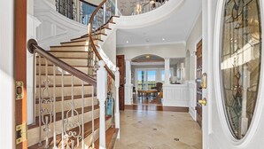 Un'imponente scalinata con ringhiere elaborate e vista su un'ampia sala da pranzo, caratterizzata da un soffitto alto e grandi finestre.
