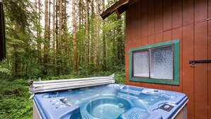 Un bain à remous situé dans une zone boisée, avec un chalet en bois en arrière-plan.
