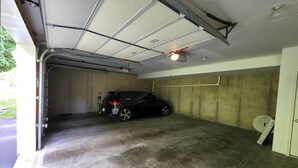 A garage with a car parked inside, concrete walls, a metal roof, and a door leading to the outside. - Idyllic carriage house private 2 car garage W/D (Newark)