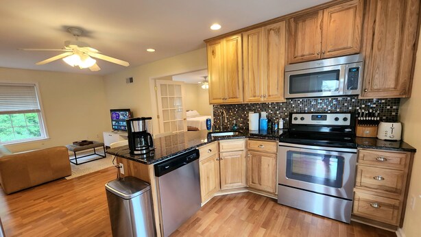 A modern kitchen with wooden cabinets, stainless steel appliances, and a central island with a dishwasher and coffee maker. - Idyllic carriage house private 2 car garage W/D (Newark)