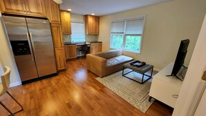 A modern kitchen with wooden cabinets, a stainless steel refrigerator, and a dining area with a sofa and ottoman. - Idyllic carriage house private 2 car garage W/D (Newark)