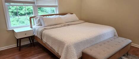 Une chambre à coucher avec un lit, une table de chevet, un banc et une fenêtre avec des stores.