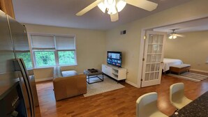 A modern living room with a flat-screen TV, a sofa, a coffee table, and a dining area with chairs. - Idyllic carriage house private 2 car garage W/D (Newark)
