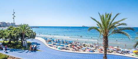 Um resort à beira-mar com piscina, guarda-sóis e palmeiras.
