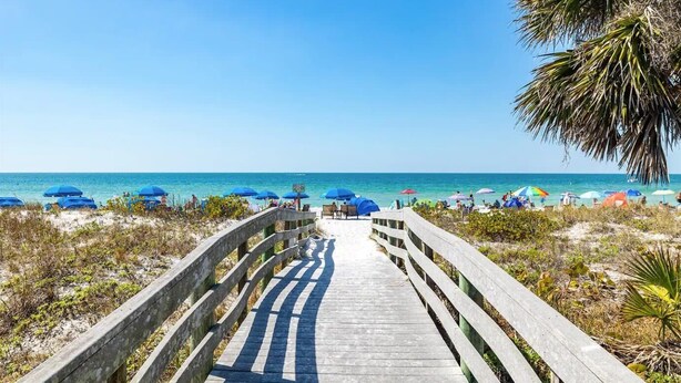 A wooden boardwalk leading to a beach with umbrellas and people.