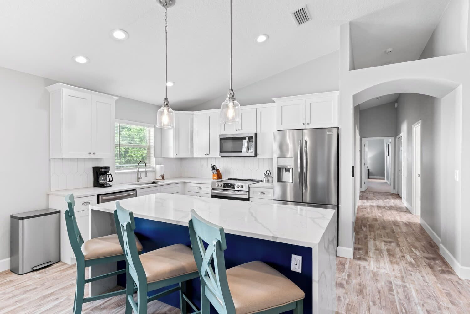 A modern kitchen with white cabinets, a large island with bar stools, stainless steel appliances, and pendant lighting.