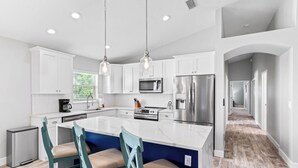 A modern kitchen with white cabinets, a large island with bar stools, stainless steel appliances, and pendant lighting.