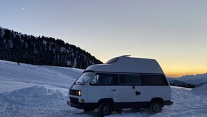 Een witte bus geparkeerd op een met sneeuw bedekte vlakte, met een berg op de achtergrond.