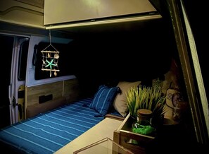 Ein gemütlicher, gut beleuchteter Schlafbereich mit Bett, Kissen und einem kleinen Tisch mit Pflanze.