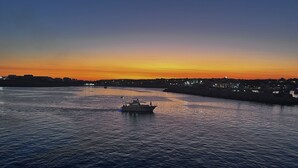 Een boot op een rustig wateroppervlak, met een stadsachtergrond in de zonsondergang.