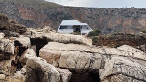 Een witte bestelwagen geparkeerd op rotsachtig terrein, met een bergachtig landschap op de achtergrond.
