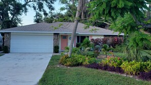 Una casa a un piano con garage, un pilastro in pietra e un giardino curato con diverse piante e una palma.