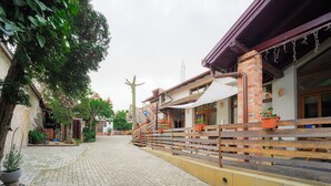 A courtyard with a paved walkway, a wooden bench, potted plants, and a building with a brick facade and a covered area.