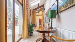 A room with a wooden dining table, a green floor lamp, and a view of the outdoors through large windows.