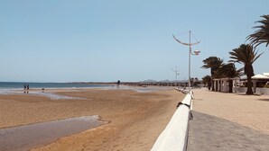 A beach with a white walkway, palm trees, and street lamps. - Apartment Alegría | Stylish accommodation right by the sea (Playa Honda)
